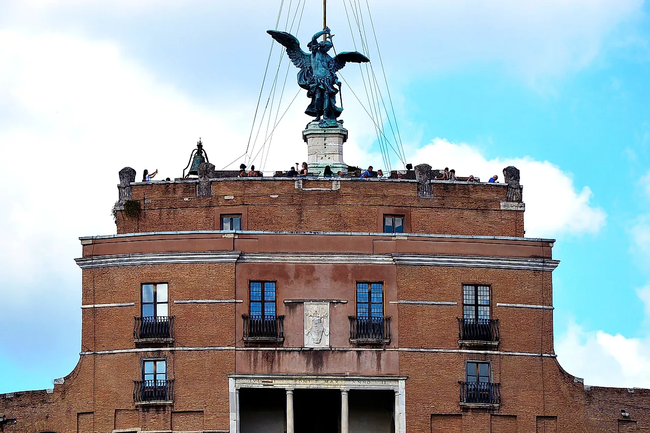 Die Spitze der Engelsburg: die Bronzestatue des Erzengels Michael mit ausgebreiteten Flügeln auf dem Gipfel, über dem oberen Backsteinblock mit seiner Loggia und der Terrasse, auf der winzige Gestalten von Besuchern stehen