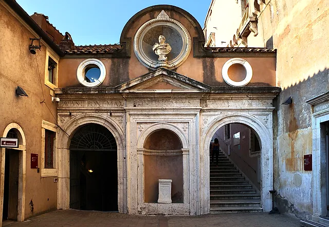 El Cortile dell'Angelo dentro del castillo: la pequeña fachada de capilla renacentista de los Santos Cosme y Damián con un busto de mármol en una hornacina redonda, dos ventanas redondas y una escalera de piedra al lado