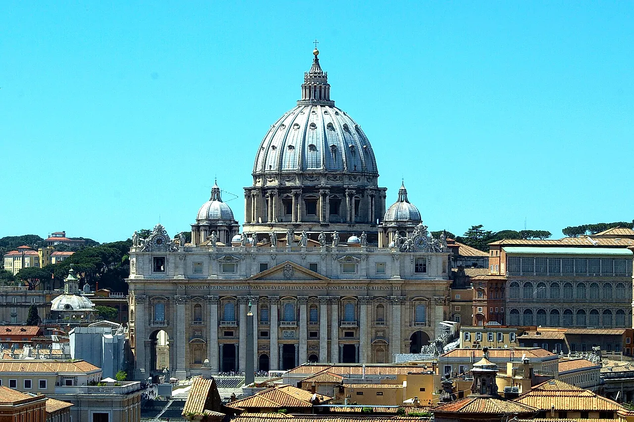 La Basílica de San Pedro y su cúpula vistas desde el Castillo de Sant'Angelo sobre los tejados de terracota del barrio del Borgo, bajo un cielo azul despejado