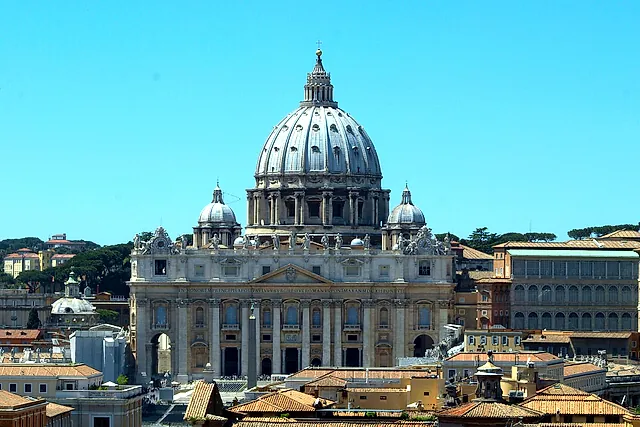 La Basílica de San Pedro y su cúpula vistas desde el Castillo de Sant'Angelo sobre los tejados de terracota del barrio del Borgo, bajo un cielo azul despejado