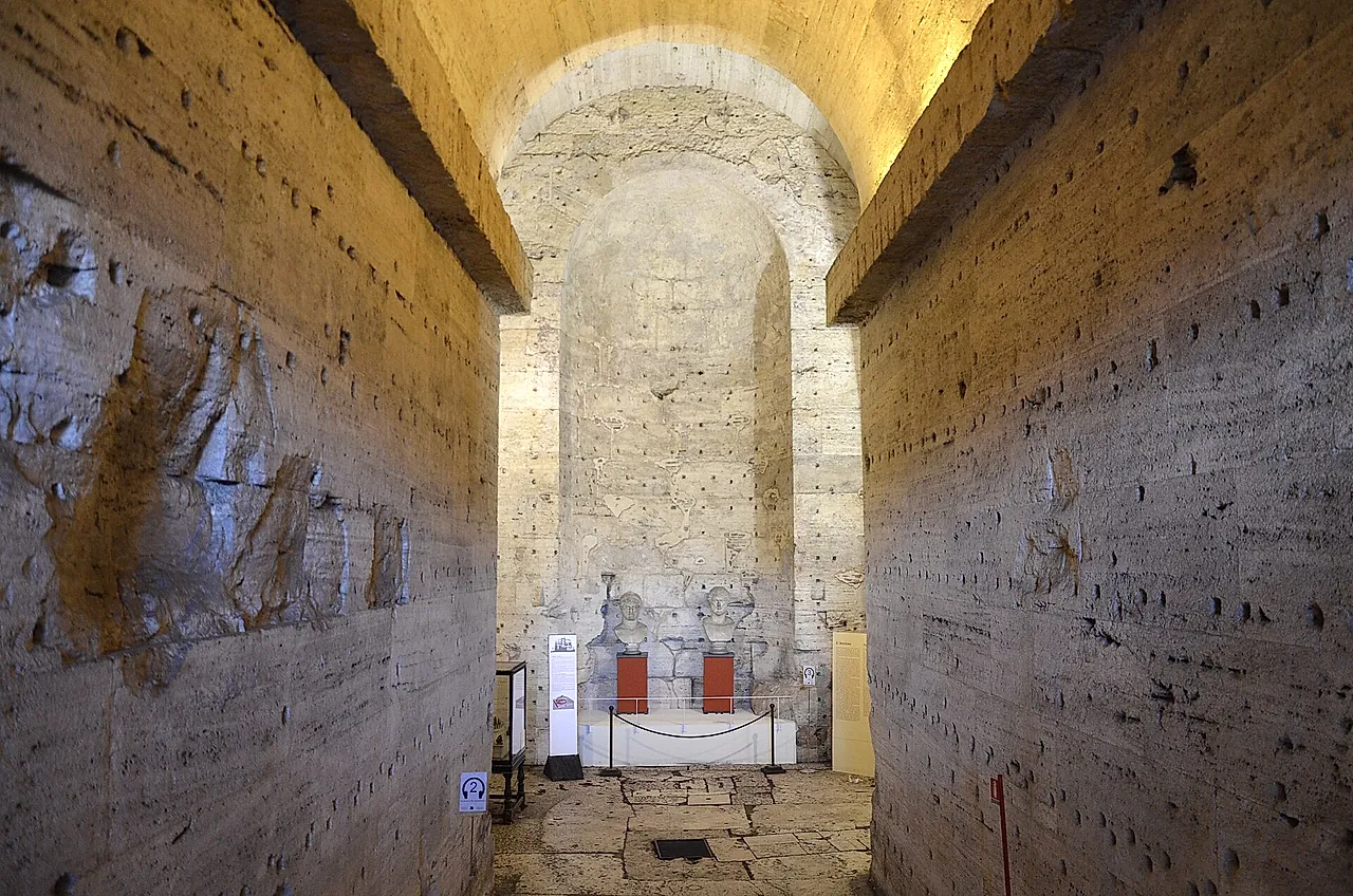 Ein langer gerader Gang aus rauem Stein und Backstein im alten Mausoleum, der zu einer beleuchteten Bogennische am Ende ansteigt, wo hinter einem Seil eine kleine Vitrine steht