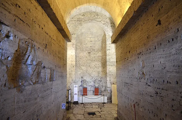 Ein langer gerader Gang aus rauem Stein und Backstein im alten Mausoleum, der zu einer beleuchteten Bogennische am Ende ansteigt, wo hinter einem Seil eine kleine Vitrine steht